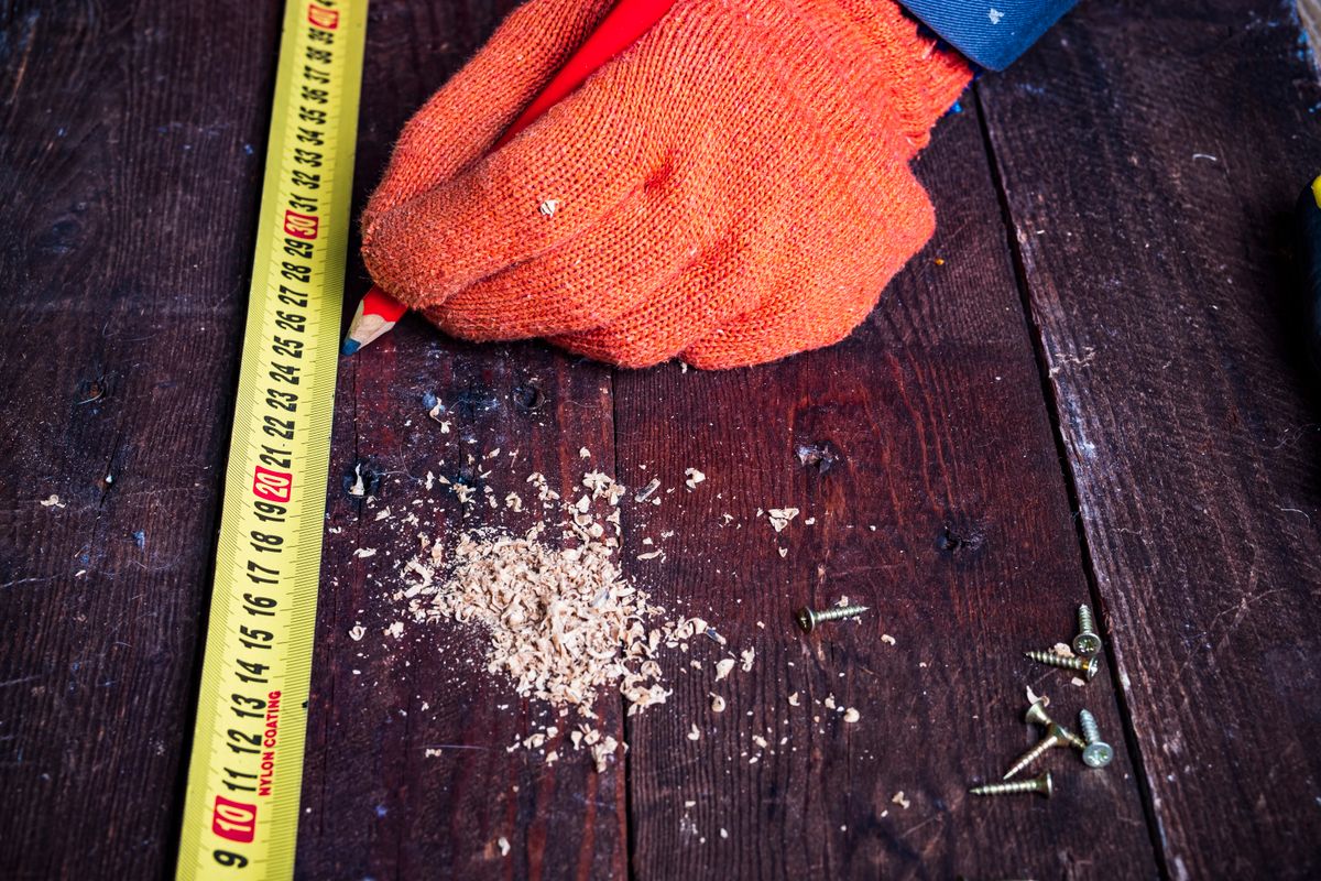 A gloved hand measuring timber beside screws and a pencil