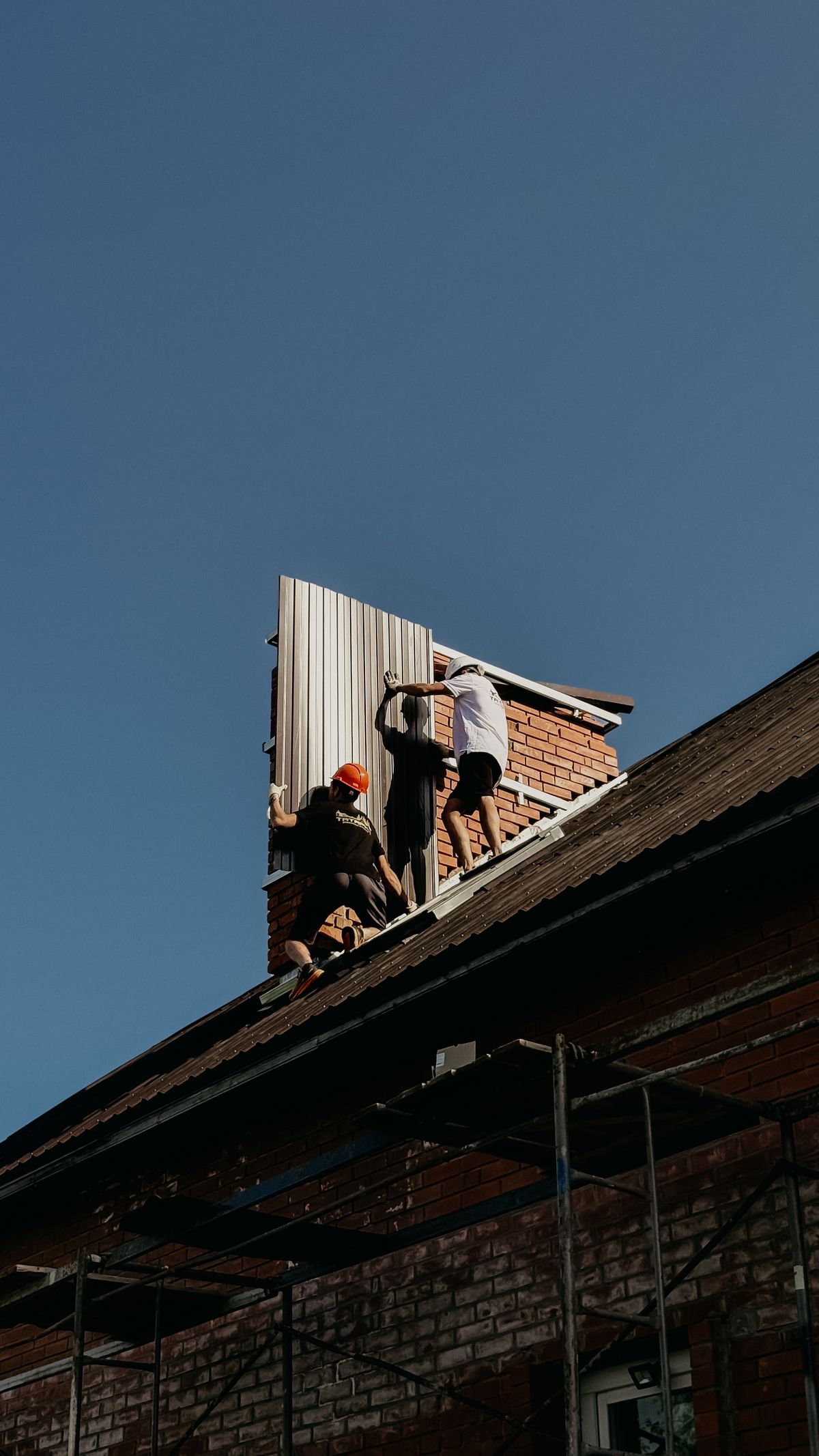 Workers fitting metal roof panels onto a house roof
