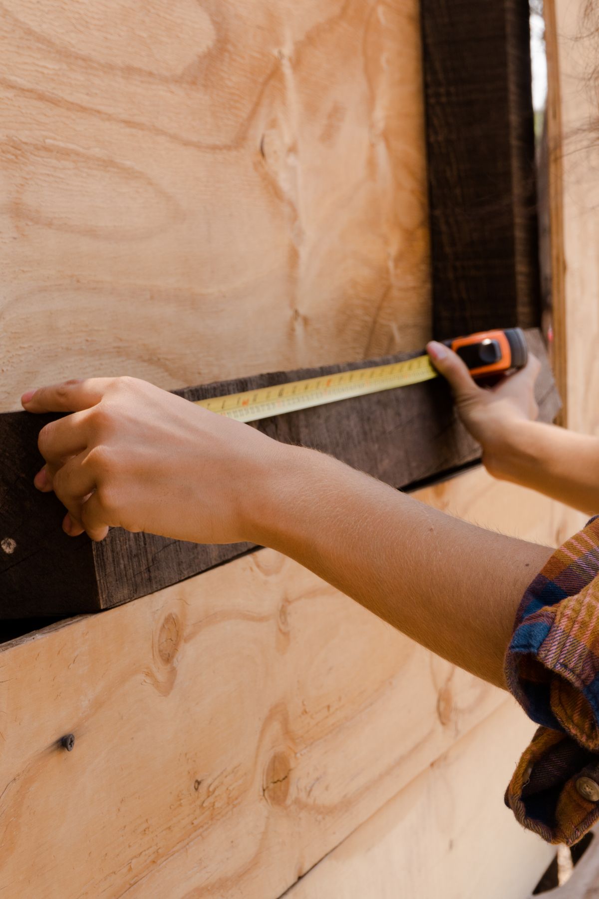 Hands measuring a piece of timber with a tape measure