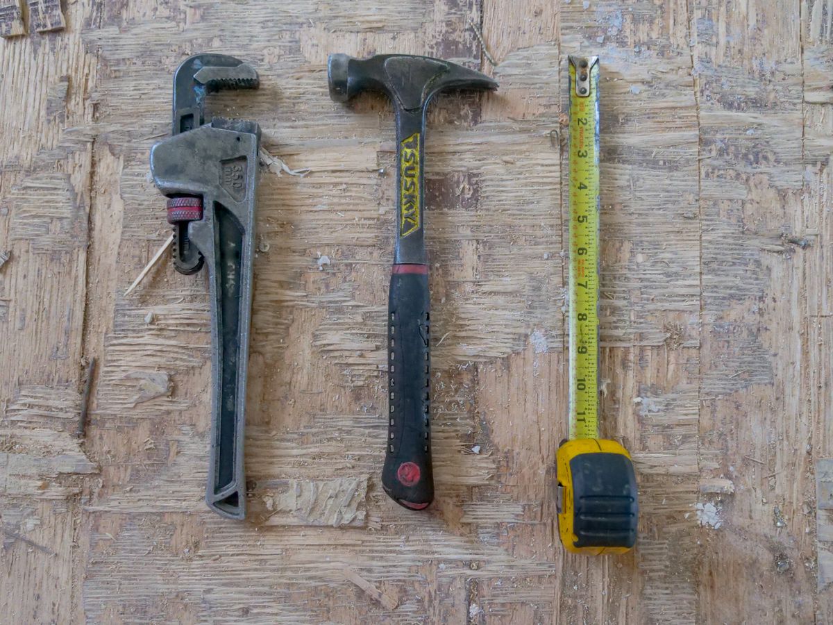 A hammer, adjustable wrench, and tape measure on a wooden work surface
